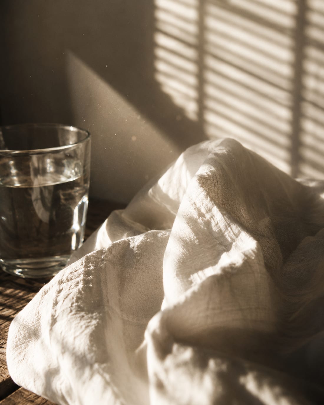 A glass of water and crumpled linen in low sun