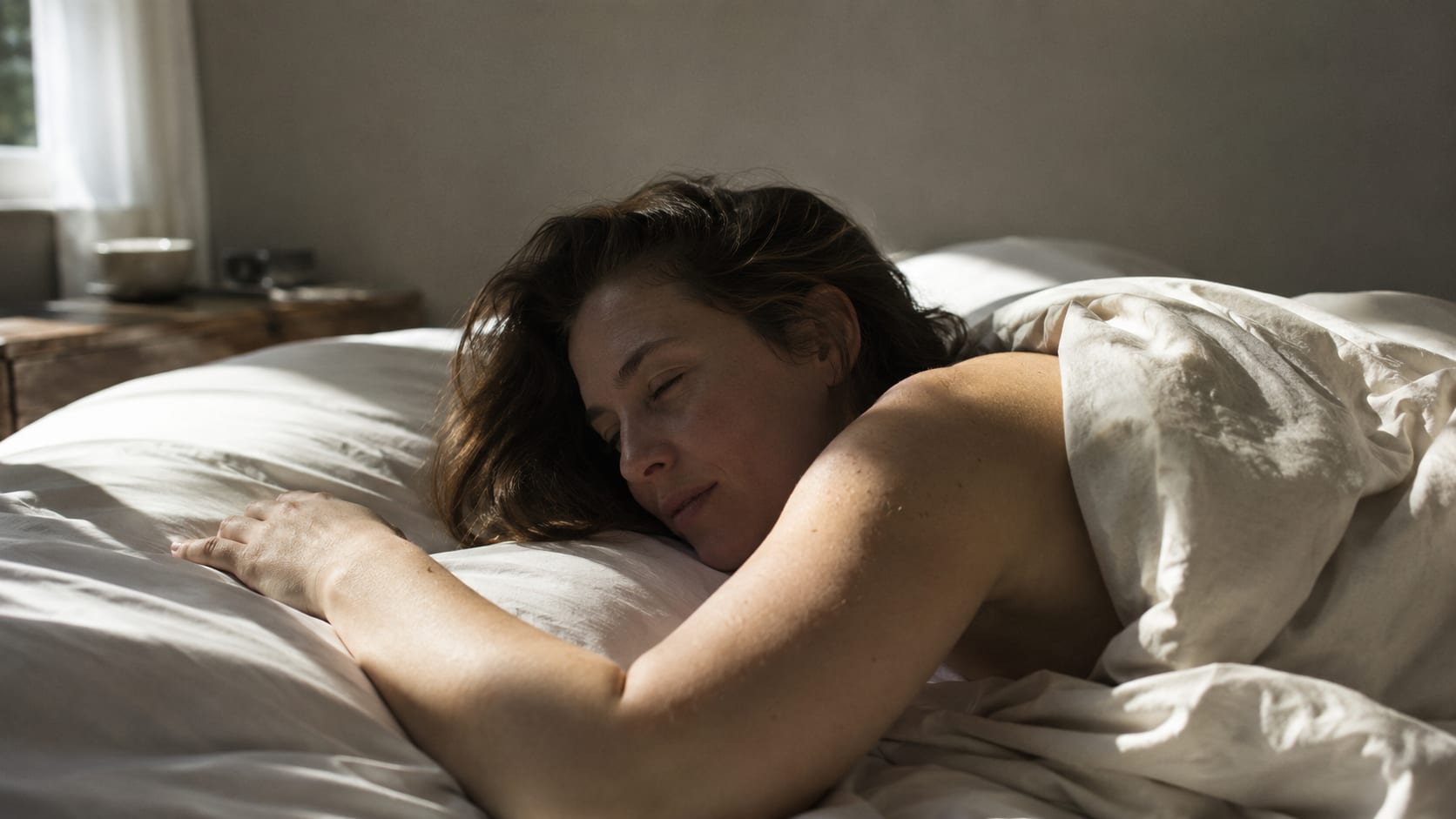 A woman asleep in white linen, first light across the bed